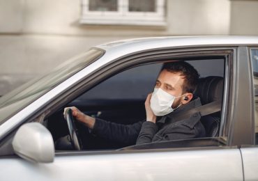 Is it illegal to drive with headphones - man wearing a mask speaking by true wireless earphones driving car on urban street.